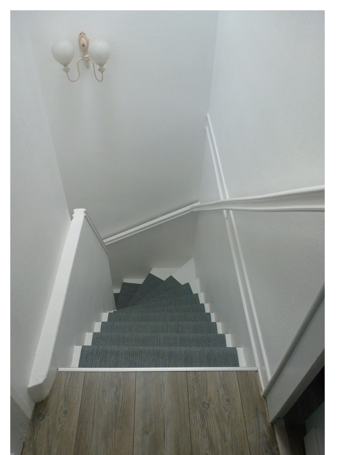 Cage d'escalier après rénovation — peinture blanche, tapis de marche gris, sol stratifié effet bois