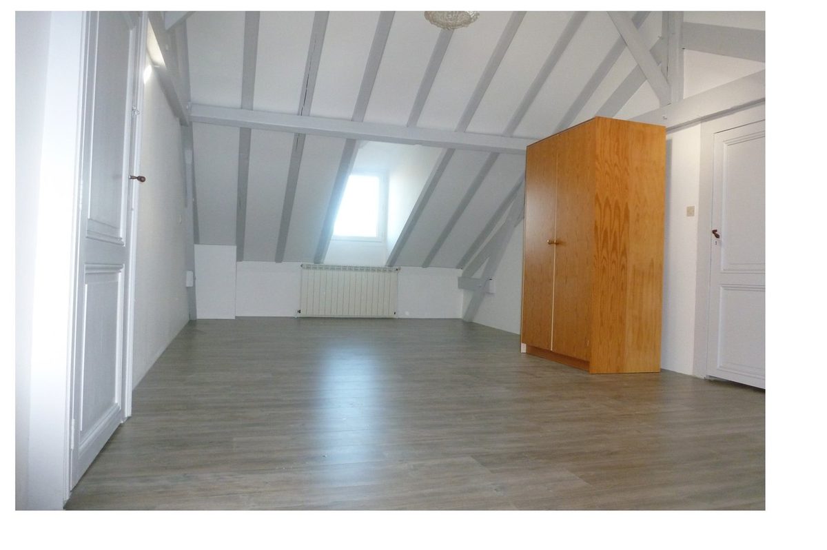 Chambre sous combles après rénovation — poutres peintes en blanc, sol stratifié gris, pièce lumineuse