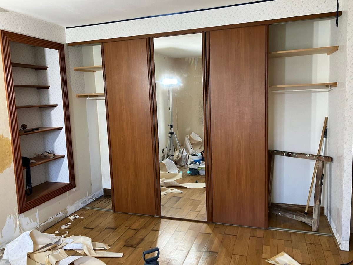 Chambre avant rénovation — papier peint fleuri d'époque et placards de style ancien avec porte-miroir